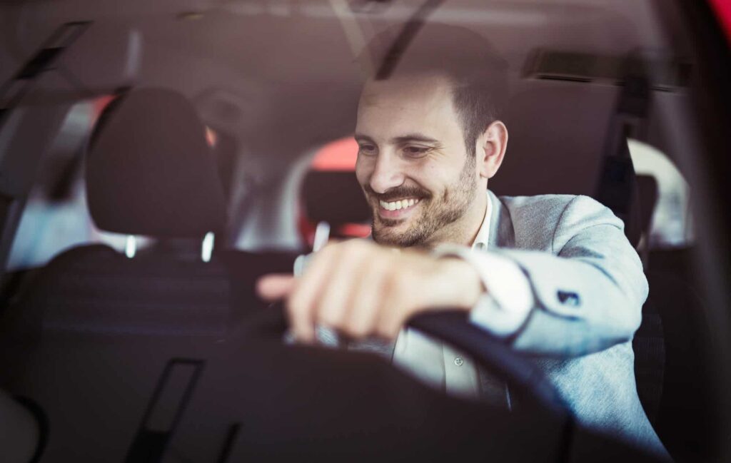 Homem dentro do carro sorrindo e dirigindo