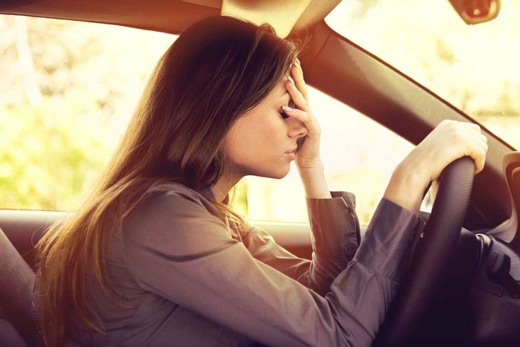 Mulher dentro do carro segurando volante com uma mão e a outra mão no rosto