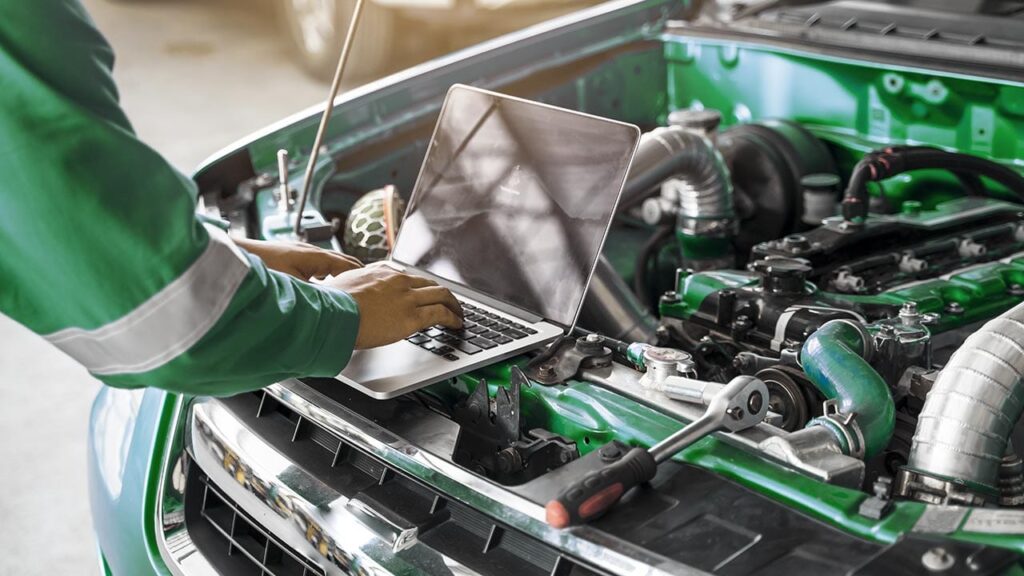 Mecânico operando um notebook sobre o motor de um automóvel