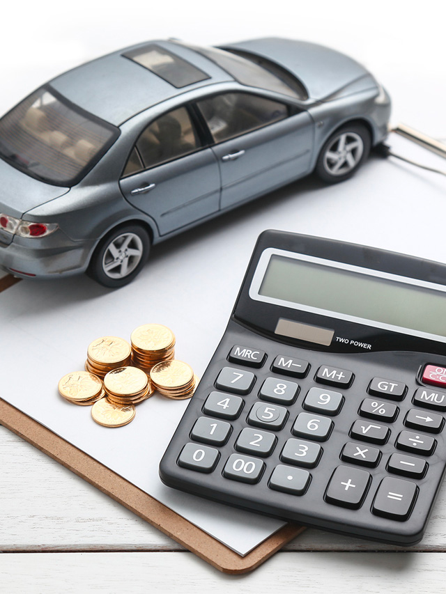Carro cinza de brinquedo sob uma prancheta com moedas e uma calculadora