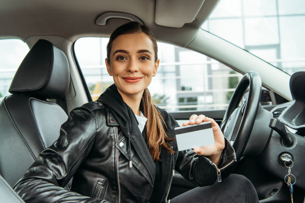 parcelar documento atrasado - mulher sorridente segura um cartão de credito na mão esquerda dentro do carro