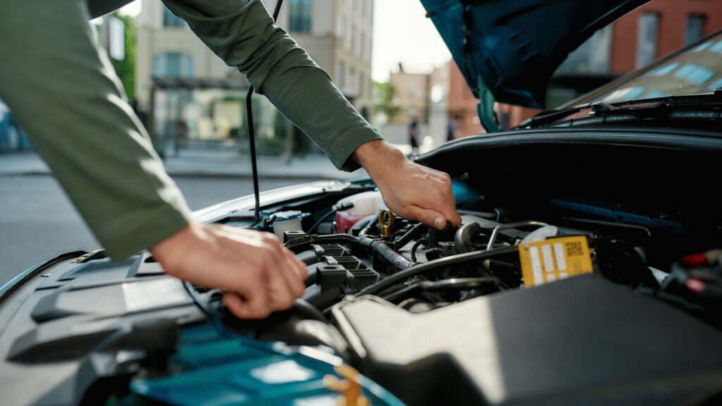 carros com manutenção barata - carro com capo aberto enquanto mao masculina mexe no motor