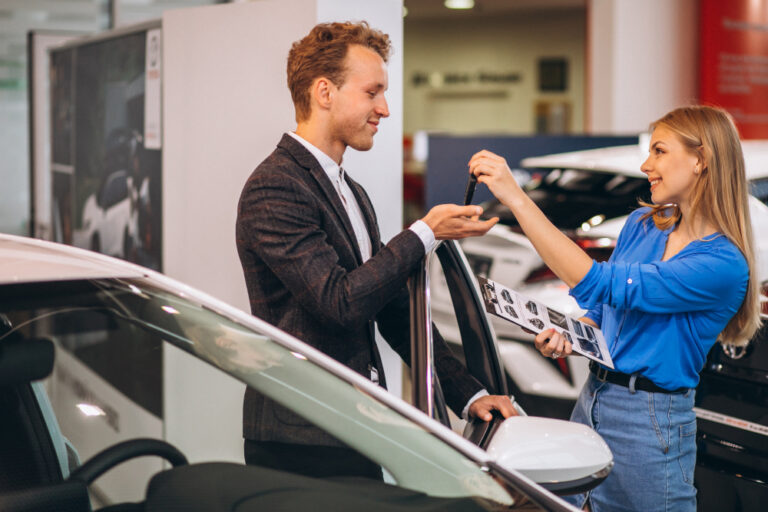 Manual do Comprador 7 como financiar carro - mulher loira vendedora de veículos entregando chave de carro para um homem