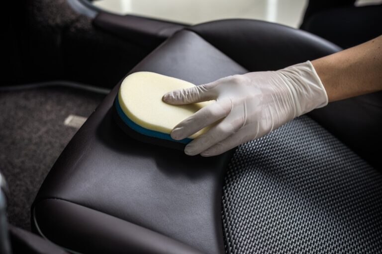 Uma pessoa que usa luvas brancas limpa um banco de couro de carro com uma esponja branca e azul