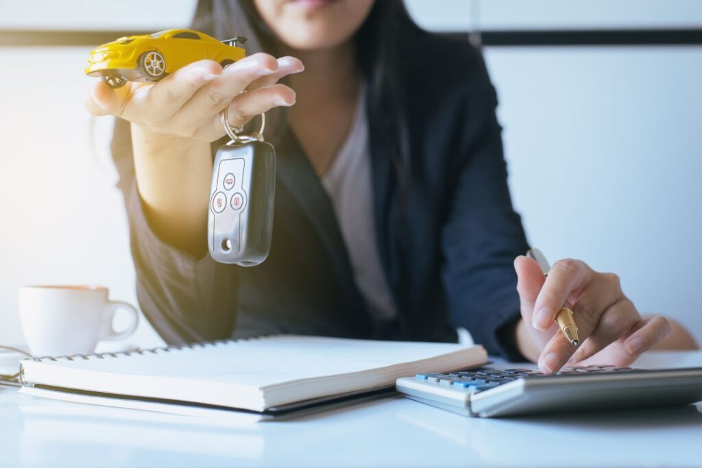 Por que os carros estão tão caros? 2 por que os carros estão tão caros - mulher segurando chave na mão e um carrinho de brinquedo amarelo e fazendo contas