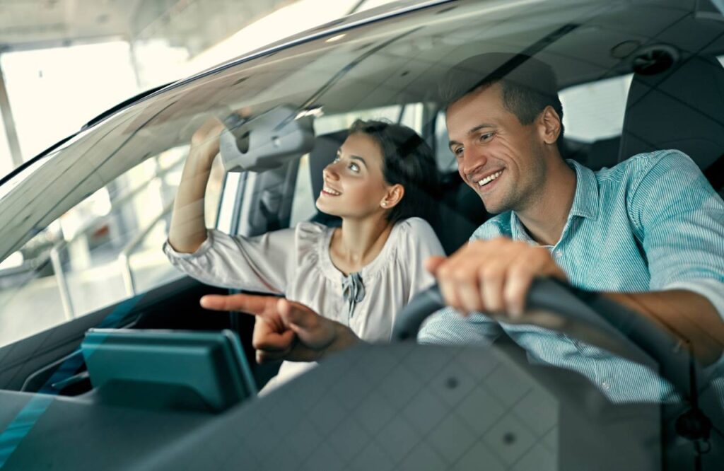 como-comprar o carro certo homem e mulher dentro de carro vendo detalhes para comprar - Como pagar menos no imposto de transferência do veículo?