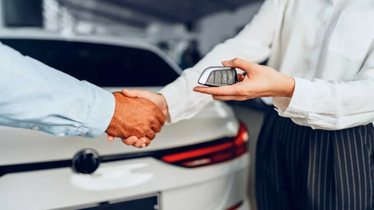 Manual do Vendedor 6 Imagem de um homem e uma mulher se cumprimentando com aperto de mãos e entregando uma chave canivete. Um carro branco ao fundo. vender carro pessoa física