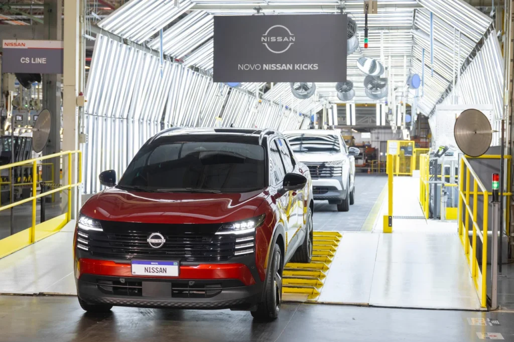 Novo Nissan Kicks vermelho lidera fila de carros saindo da linha de produção, sob o letreiro “Novo Nissan Kicks”