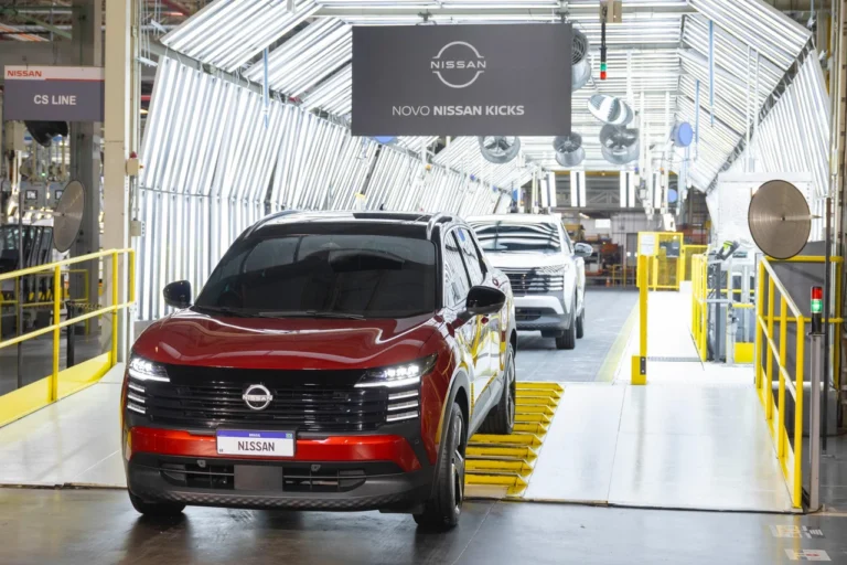 Novo Nissan Kicks vermelho lidera fila de carros saindo da linha de produção, sob o letreiro “Novo Nissan Kicks”
