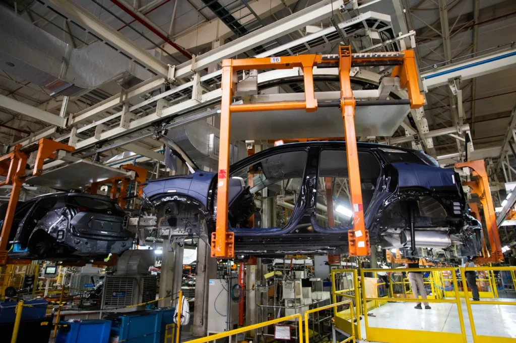 Estrutura de um carro preto em processo de montagem suspenso por braço mecânico na fábrica da Nissan.