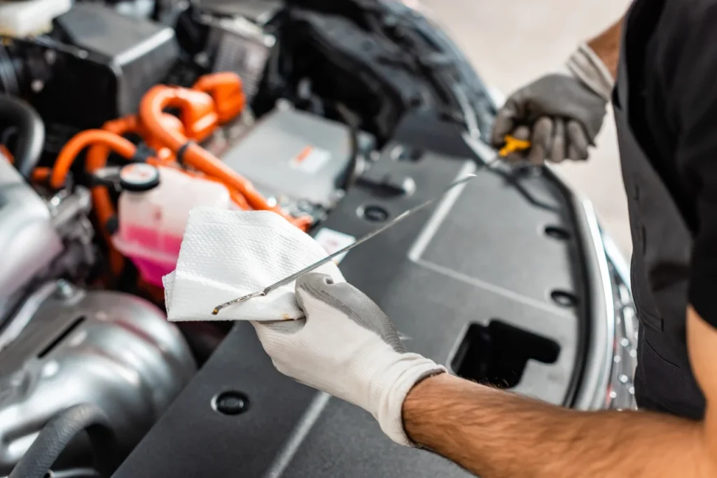 Especificações de óleo de motor: o que muda e como isso afeta seu carro 2 Mecânico verificando as especificações de óleo de motor ao inspecionar o nível com a vareta no compartimento do motor de um carro.