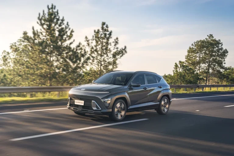 Hyundai Novo KONA Hybrid em movimento em estrada cercada por árvores, sob céu limpo