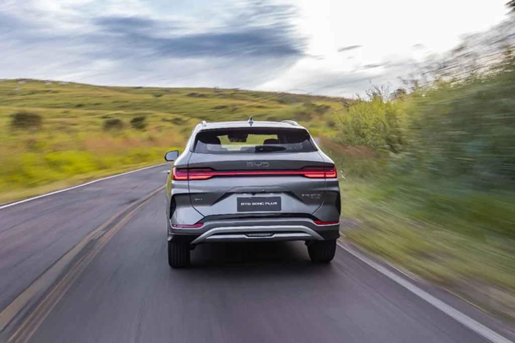 Novo BYD Song Plus 2026: head-up display e novo visual por R$ 249.990 3 Vista traseira do BYD Song Plus 2026 em movimento em uma estrada sinuosa no campo.