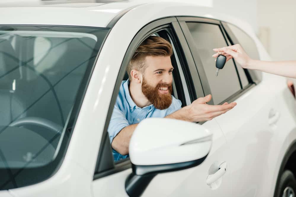 Homem dentro de um carro branco recebendo a chave do veículo