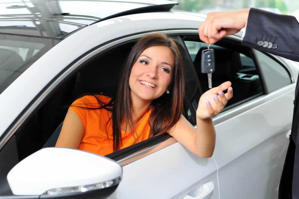 Mulher sorrindo dentro do carro e pegando uma chave que um homem está entregando