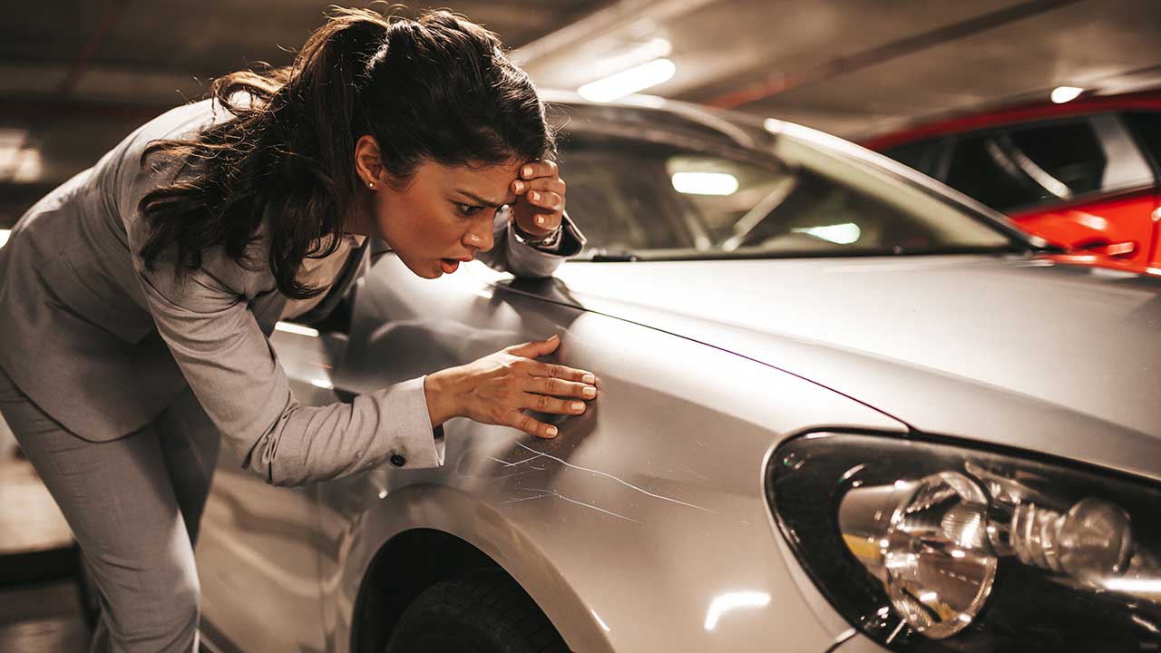 Mulher inconformada olhando a lataria arranhada de um carro prata