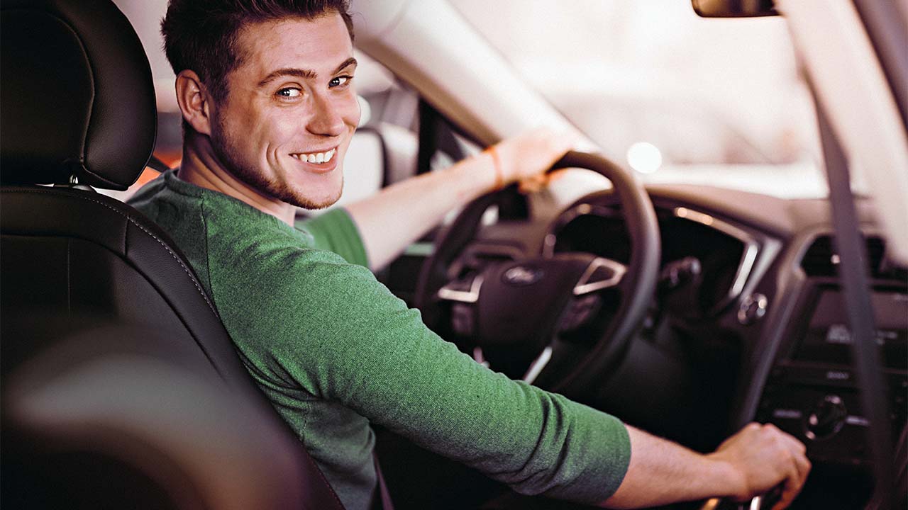 Homem sorridente na direção de um carro automático