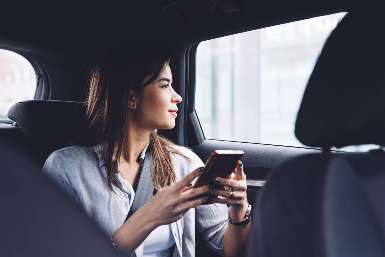 como atrair clientes para as redes sociais - mulher sentada no banco de trás de um carro olhando para fora e com celular na mão