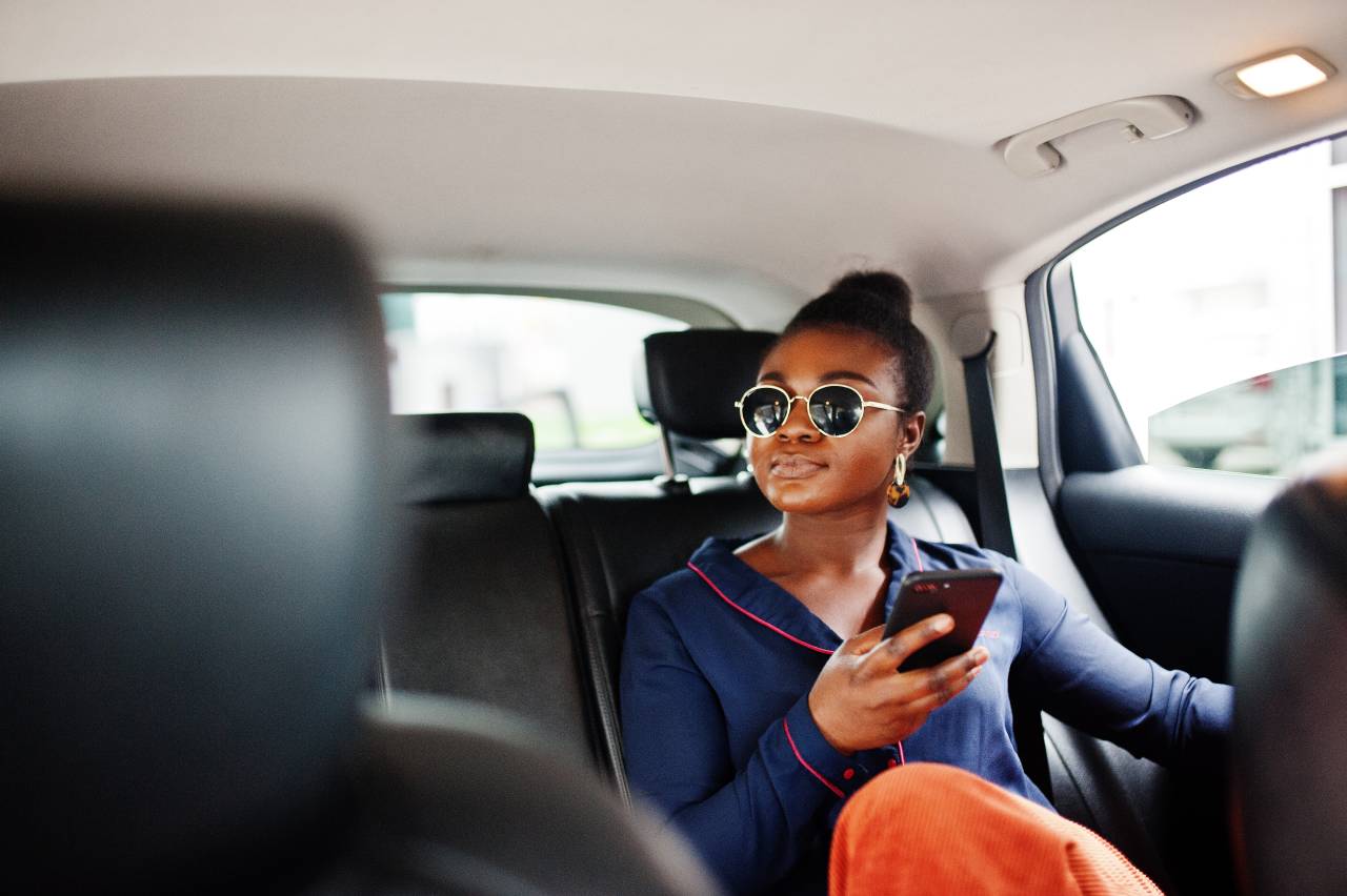 como atrair clientes pelas redes sociais - mulher usando celular no banco de trás de um carro e usando óculos escuros